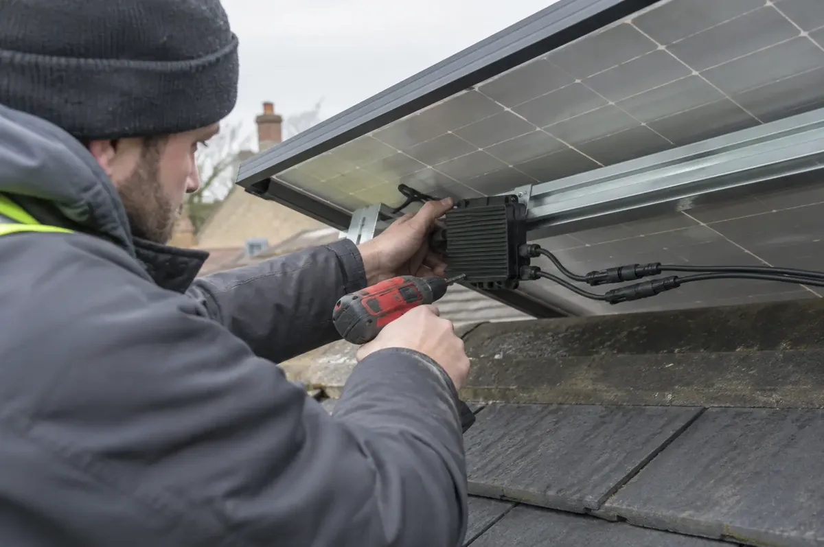 Installer fastening a small black solar power optimiser with paired cables beneath a panel.